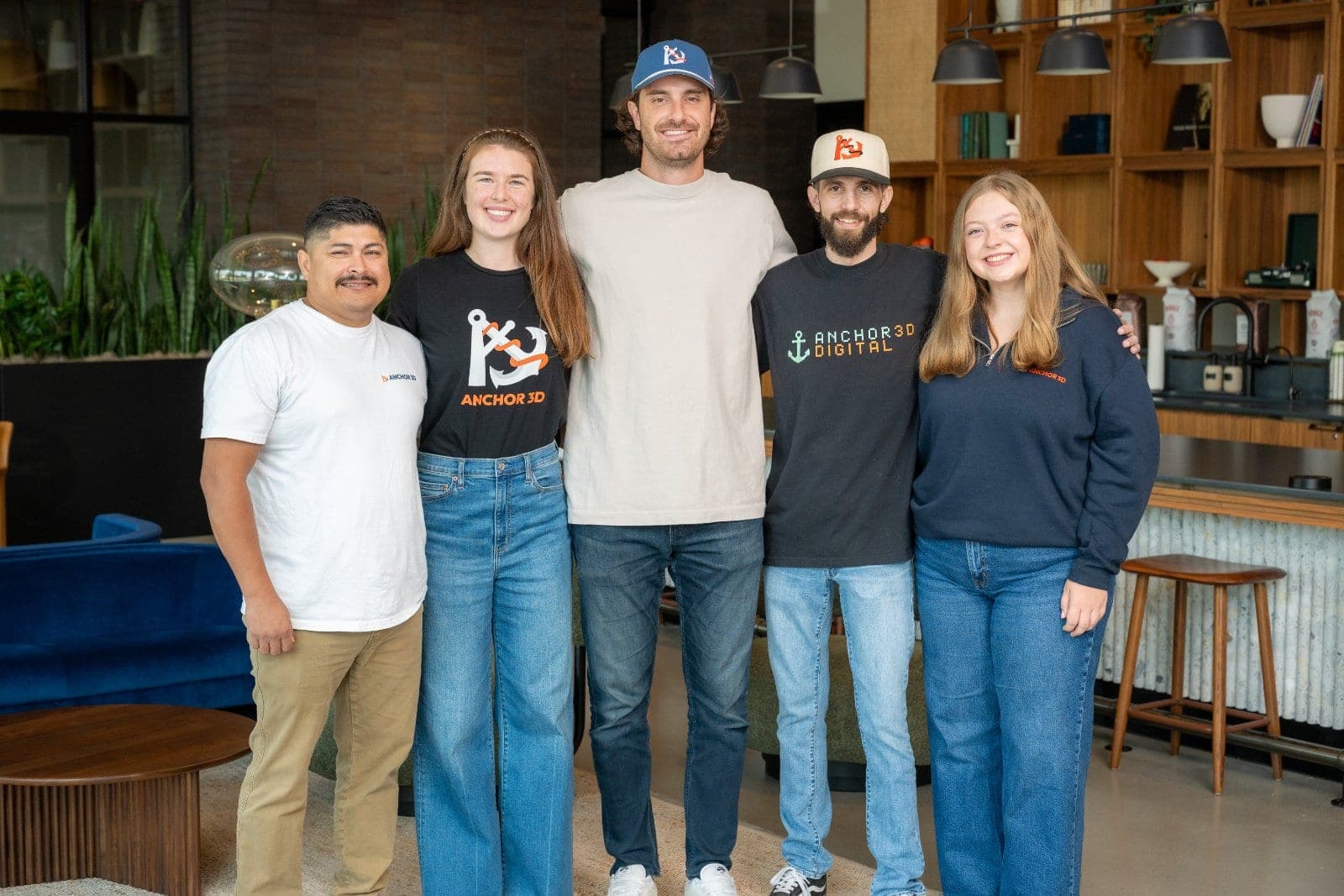 Five team members standing together and smiling for a group portrait inside a modern workplace.