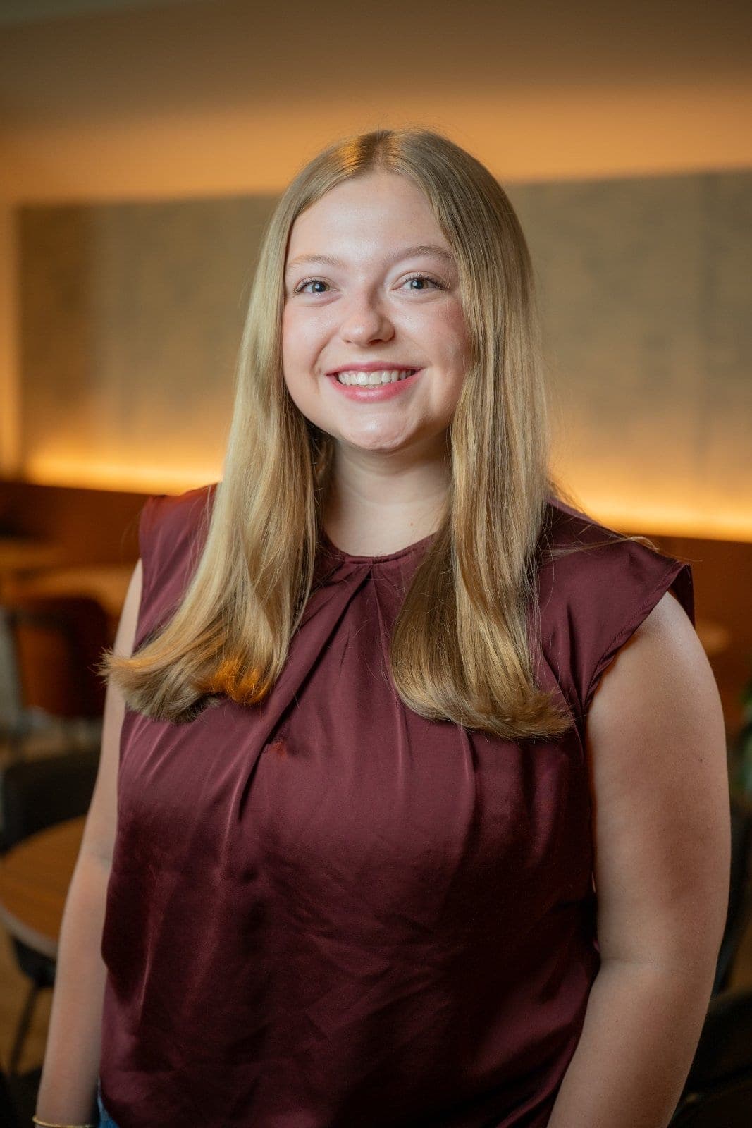 Professional portrait of a smiling woman photographed indoors with a softly blurred office background.