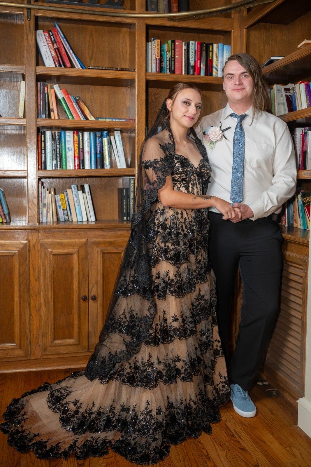 Wedding couple holding hands and posing together in front of wooden bookshelves during their Marble Falls wedding.