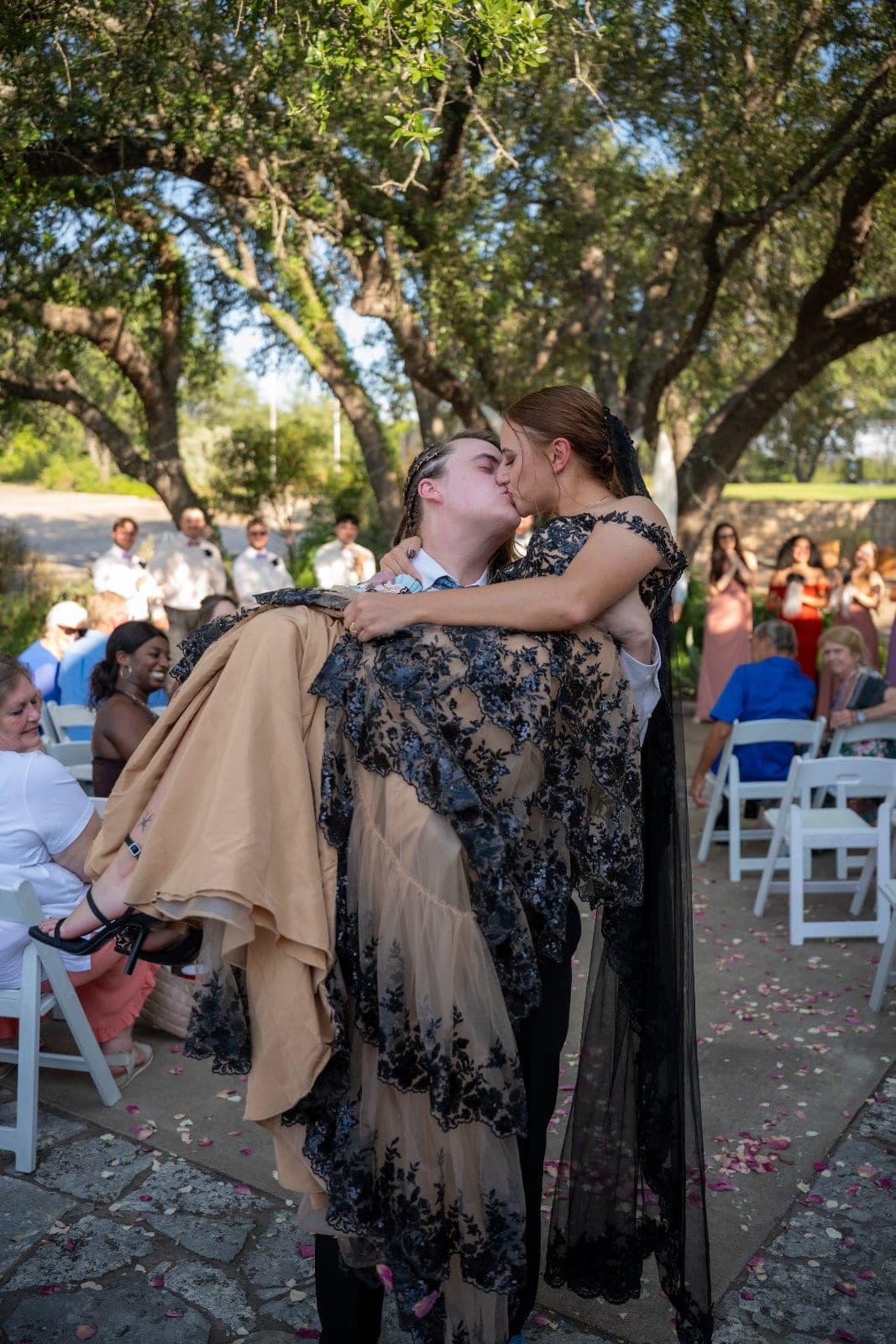 Newlywed couple sharing a kiss as one partner carries the other down the aisle during an outdoor wedding celebration in Marble Falls, Texas.