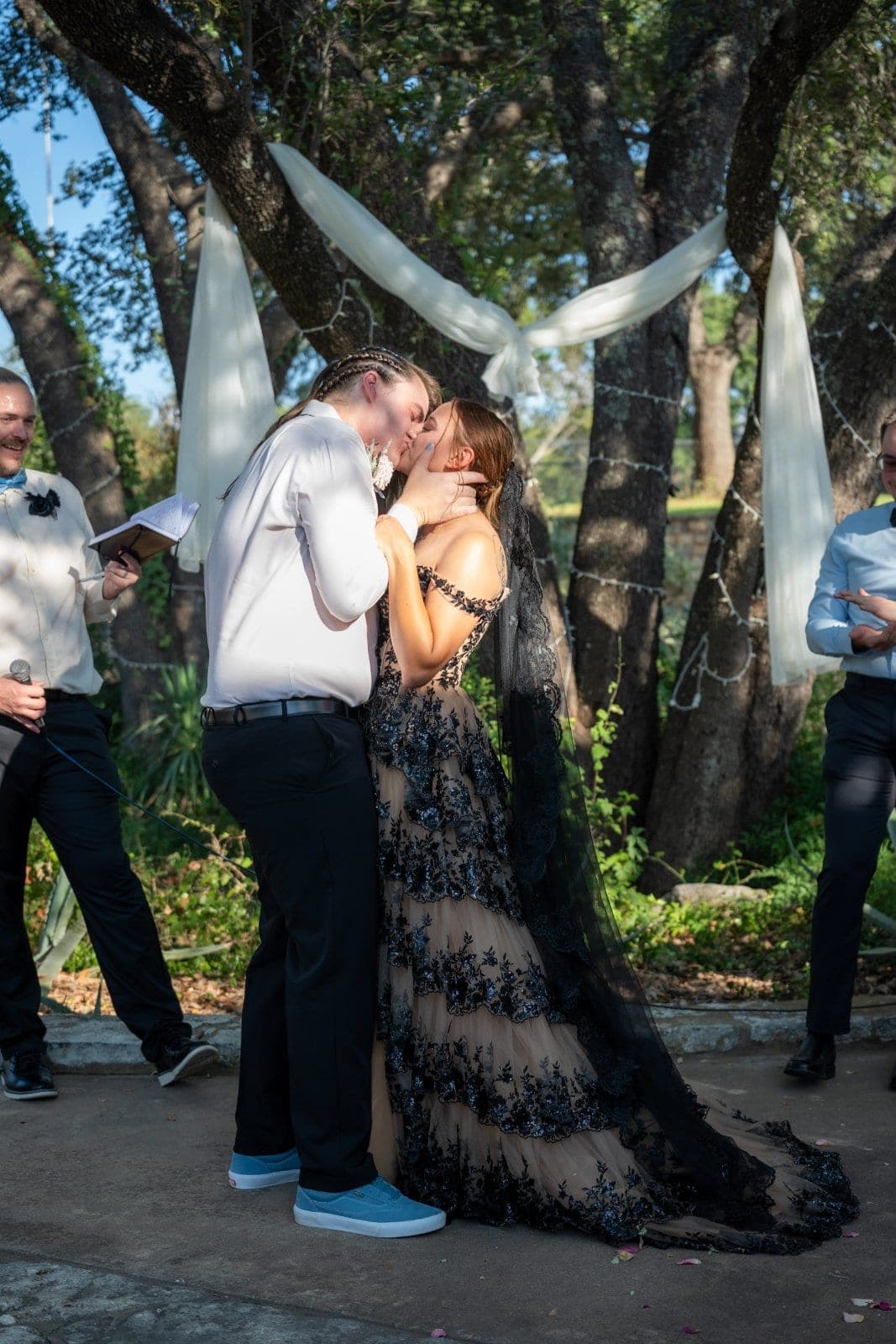 Wedding couple sharing a kiss during their outdoor ceremony beneath trees and white draping in Marble Falls, Texas.