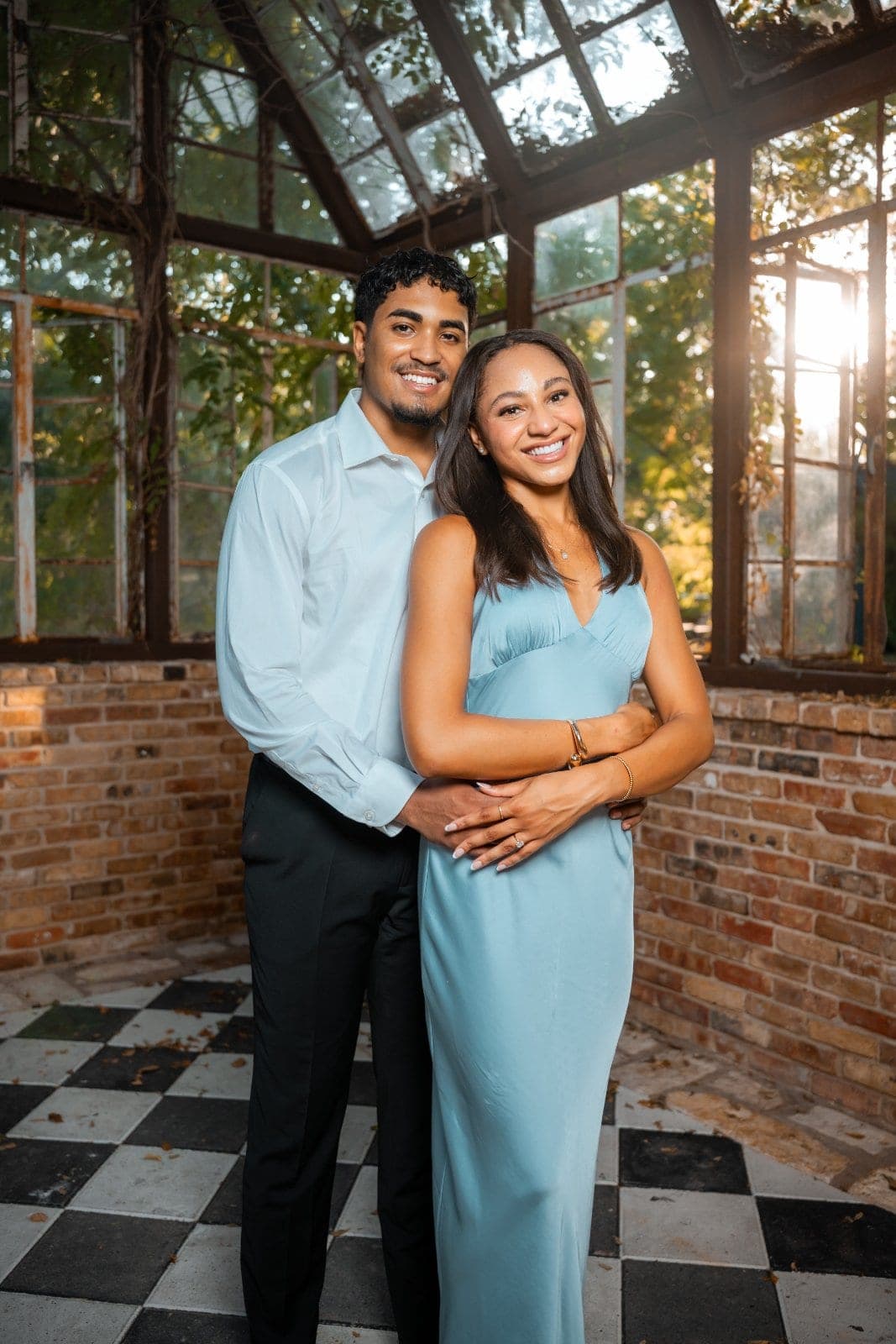 Newly engaged couple smiling together inside a rustic glass greenhouse during their engagement photography session in Austin, Texas.