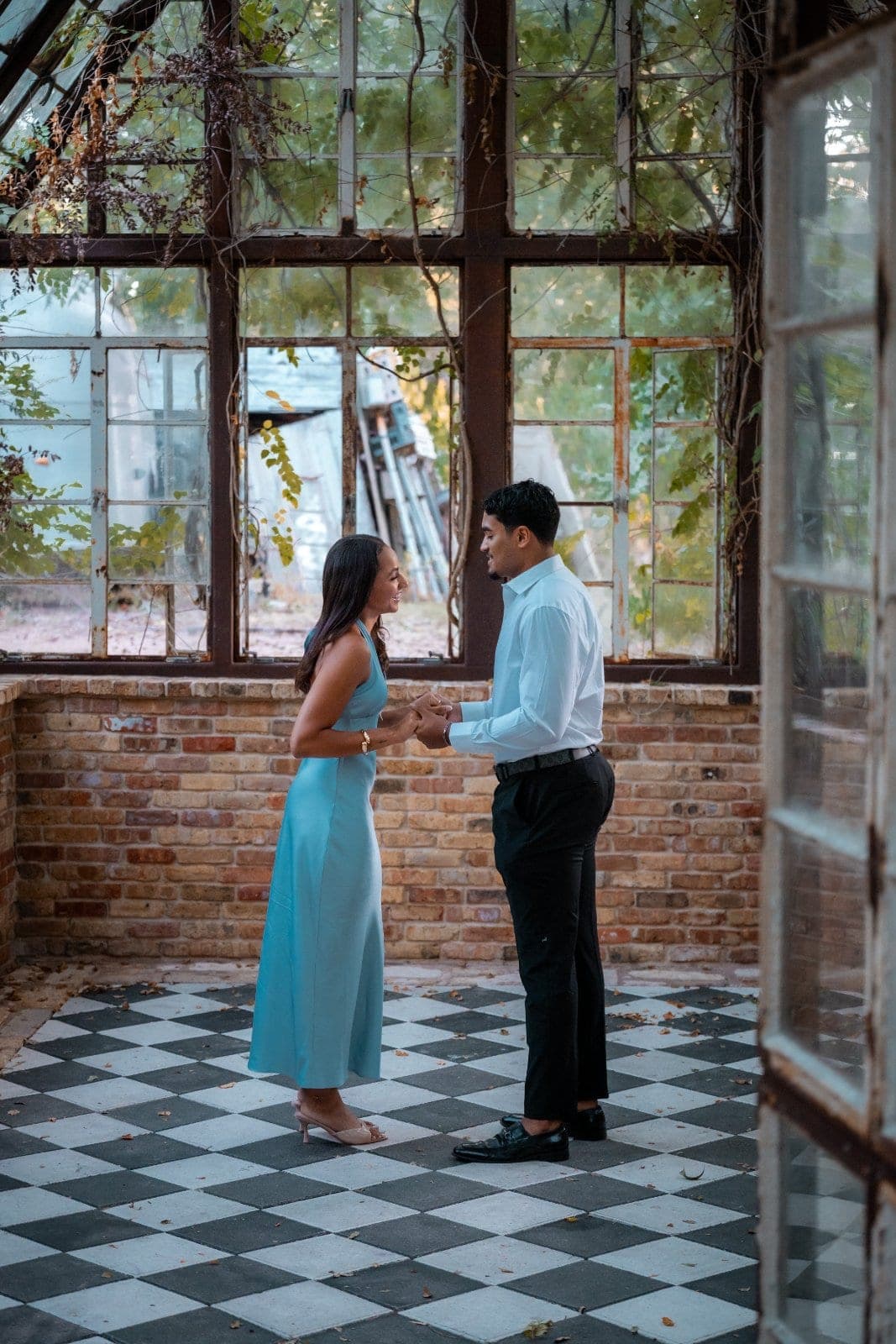 Newly engaged couple holding hands and smiling at each other inside a greenhouse moments after their Austin proposal.