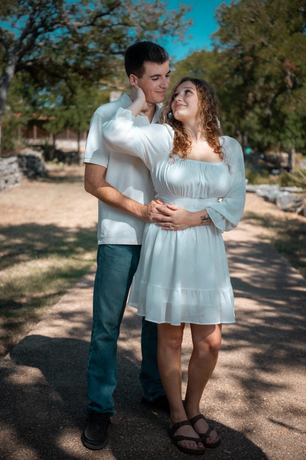 Engaged couple embracing and smiling at each other during an outdoor portrait session in Burnet, Texas.