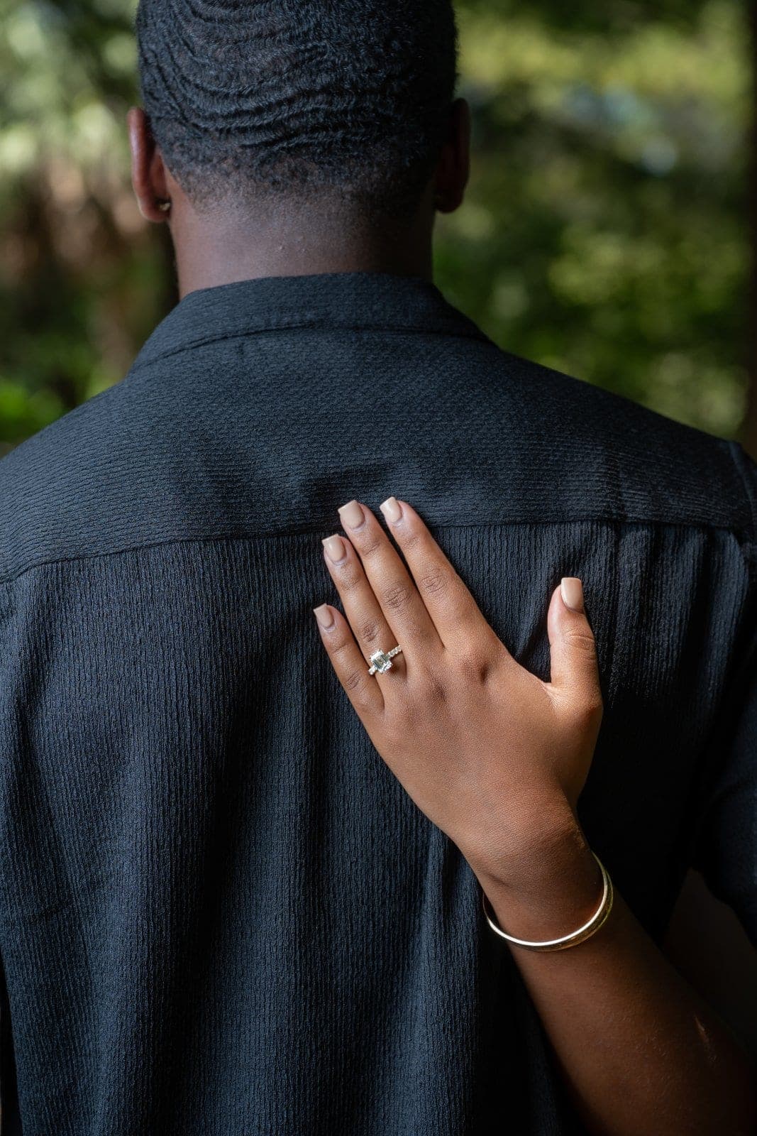 Newly engaged woman displaying her engagement ring while resting her hand on her partner’s shoulder during an outdoor proposal session.