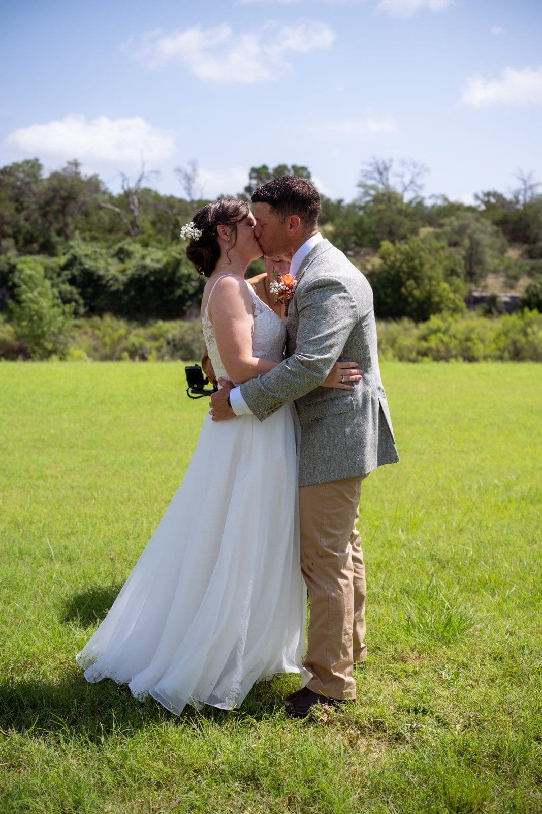 Bride and groom sharing a romantic kiss in a sunny field on their wedding day in Austin, Texas.